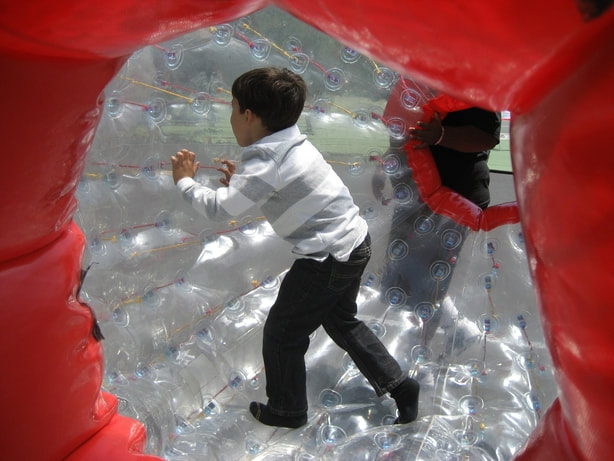 Young boy walking inside large blow up ball known as a hamster ball 
