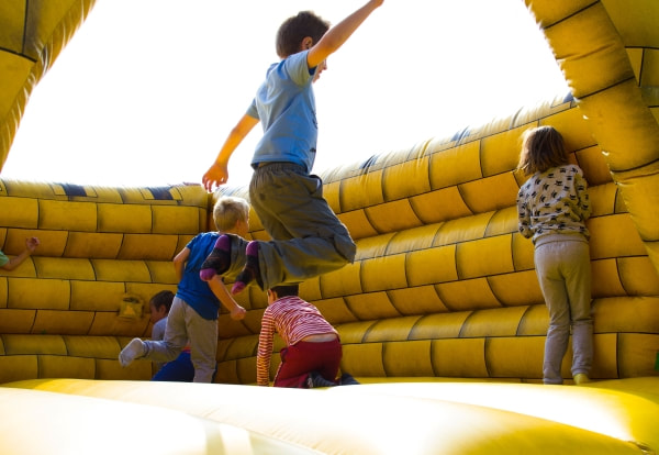 children playing in a yellow brick bouncy castle while one boy jumps